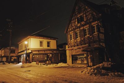 Houses by snow covered street against sky at night