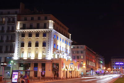 Illuminated buildings by road against sky in city at night