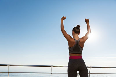 Woman exercising while standing against sea and sky