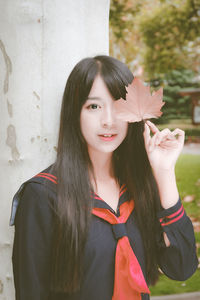 Portrait of smiling young woman standing against wall