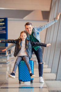 Portrait of father and daughter with arms outstretched at airport