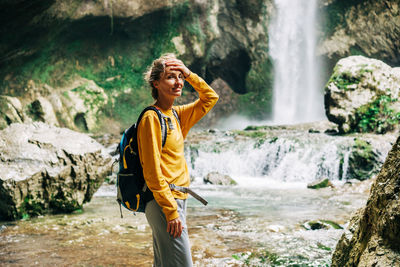 Happy caucasian woman walking near the waterfall smiling and enjoying the freshness on a summer day.