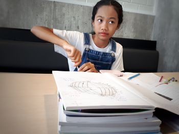 Girl looking away while studying on table at home