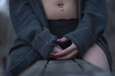 Midsection of woman wearing sweater while sitting on wooden bench