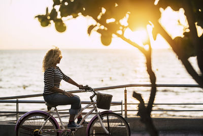 Side view of woman riding bicycle by sea against sky