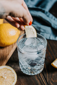 Close-up of woman putting lemon in drink on table