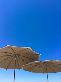 Low angle view of parasols against clear blue sky