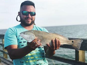 Man holding fish at pier against sky