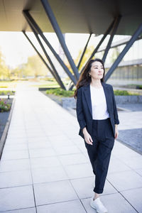 Full body portrait of asian confident business woman in suit, walking in business center spring park