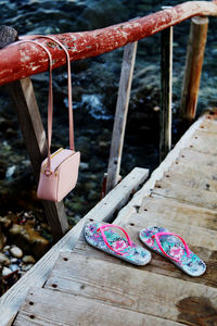 High angle view of flip-flops on wooden bridge by bag hanging on railing