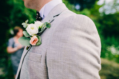 Midsection of bridegroom with flower on suit standing outdoors
