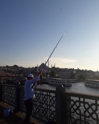 Rear view of man standing by river in city against sky