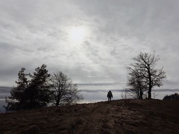 Rear view of silhouette man walking on field against sky