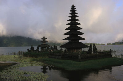 Pagoda by lake against cloudy sky