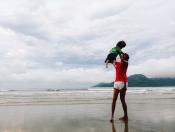 Mother holding son at beach against cloudy sky