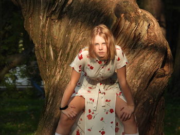 Portrait of young woman standing by tree trunk