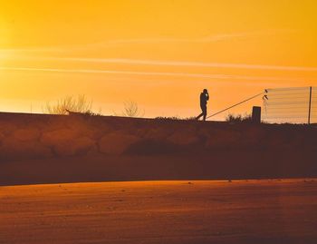 Silhouette man standing on shore against sky during sunset