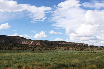 View of green field with rocky mountain range against cloudy sky