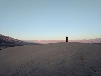 Silhouette man standing on sand dune against clear sky