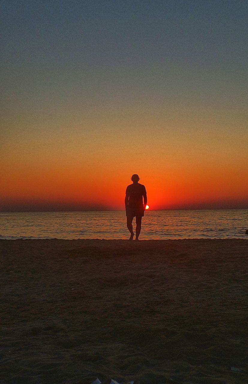 SILHOUETTE MAN STANDING ON BEACH DURING SUNSET