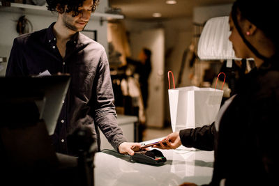 Side view of female customer paying through smart phone at store