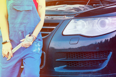 Midsection of woman with wrench leaning on car
