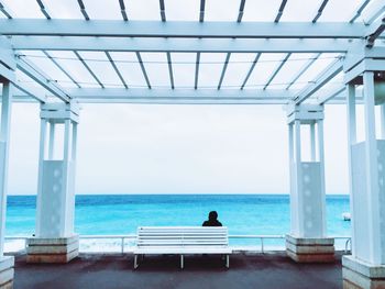 Rear view of man sitting on bench in gazebo against sea