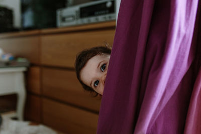 Portrait of cute baby girl peeking from behind curtain