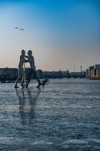 Men by sea against sky during sunset