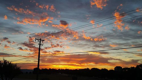 Low angle view of silhouette electricity pylon against sky during sunset