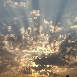 Low angle view of sunlight streaming through clouds