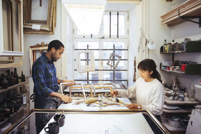 Male craftsperson making frame with female coworker at workbench in store