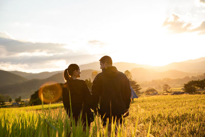 Rear view of couple standing at farm against sky during sunset