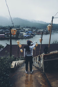 Rear view of man looking at cityscape by river against mountains