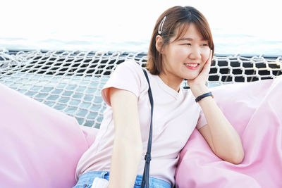 Portrait of a smiling young woman sitting against pink water