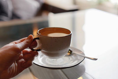 Closeup of female hands with french manicure holding cozy ceramic white mug of tea or coffee.