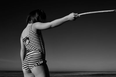 Woman holding umbrella while standing by sea against clear sky