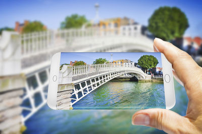 Person holding umbrella by bridge against sky