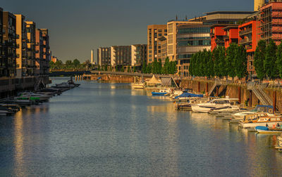 Boats moored in river by buildings in city against sky