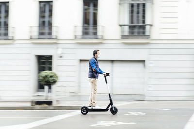 Young man wearing protective face mask riding electric push scooter on street in city