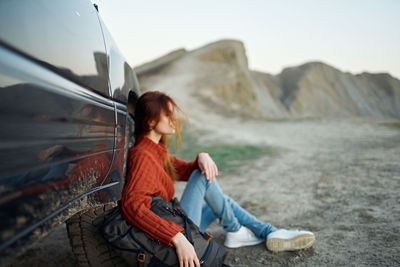 Full length of woman sitting on rock against mountain