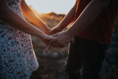 Midsection of couple holding hands during sunset