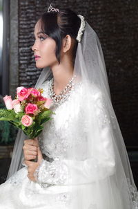 Bride holding bouquet sitting against wall