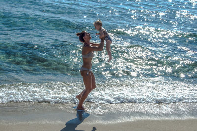 Full length of playful mother lifting daughter while standing on shore at beach during summer