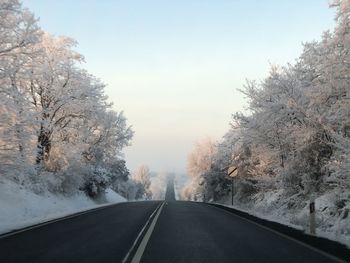 Road amidst trees against sky during winter