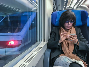 Woman using phone in illuminated subway train