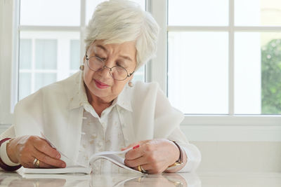 Senior woman reading book while sitting at home