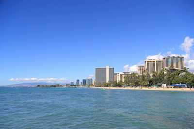 Buildings by sea against blue sky