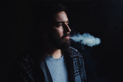 Portrait of man smoking cigarette against black background