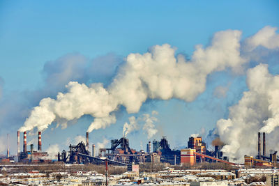 Smoke emitting from factory against cloudy sky